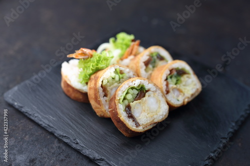 Tempura maki rolls with shrimp, lettuce, cucumber and pickled radish. 6 piece sushi set in Japanese omelette, on a black stony background. Japanese cuisine delicacy.