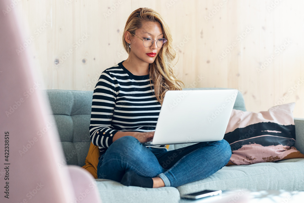 Beautiful asian business woman working and typing with laptop while sitting on couch in coworking place. Beautiful asian business woman working and typing with laptop while sitting on couch in coworking place.