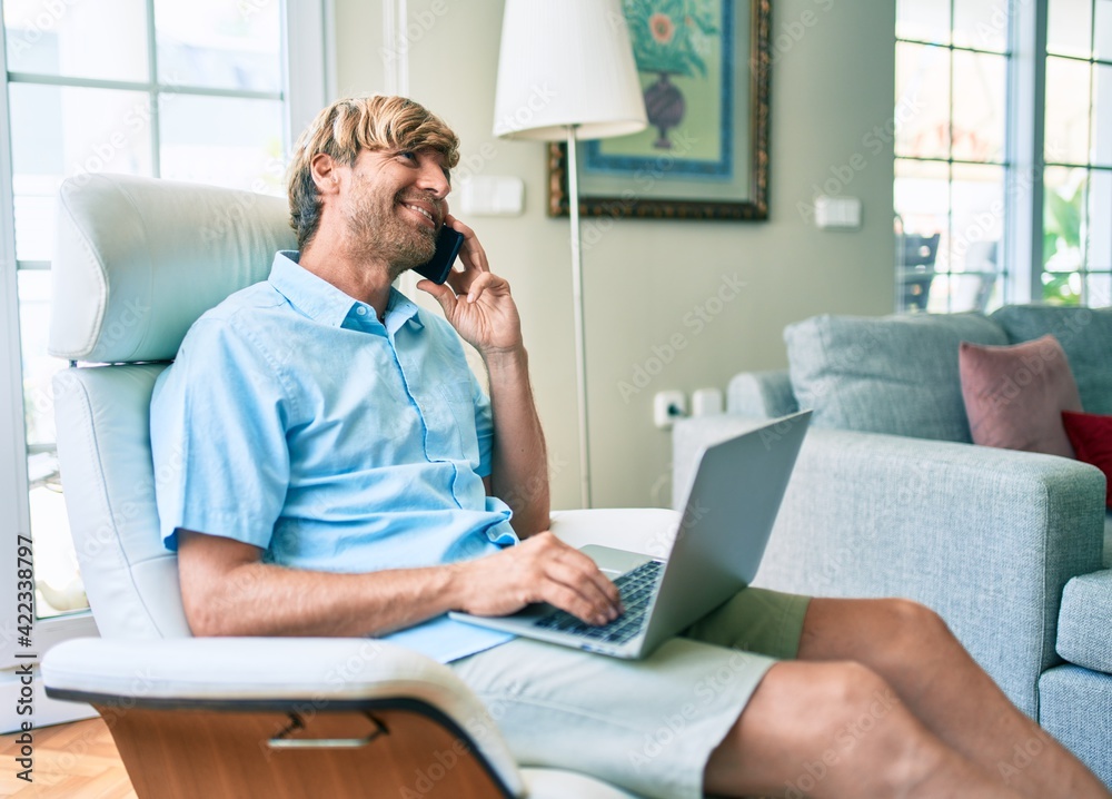 Middle age handsome caucasian man relaxing at home working with computer laptop on the sofa speaking on the phone Middle age handsome caucasian man relaxing at home working with computer laptop on the sofa speaking on the phone