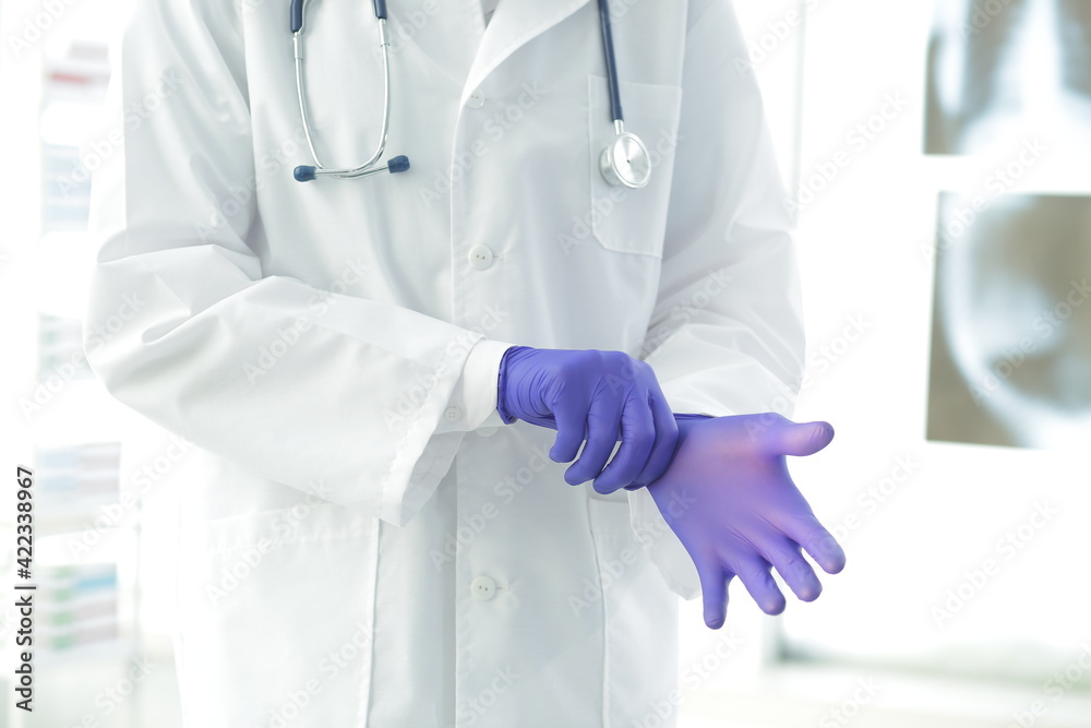 Doctor with stethoscope in a medical gown puts on protective gloves in a clinic Doctor with stethoscope in a medical gown puts on protective gloves in a clinic