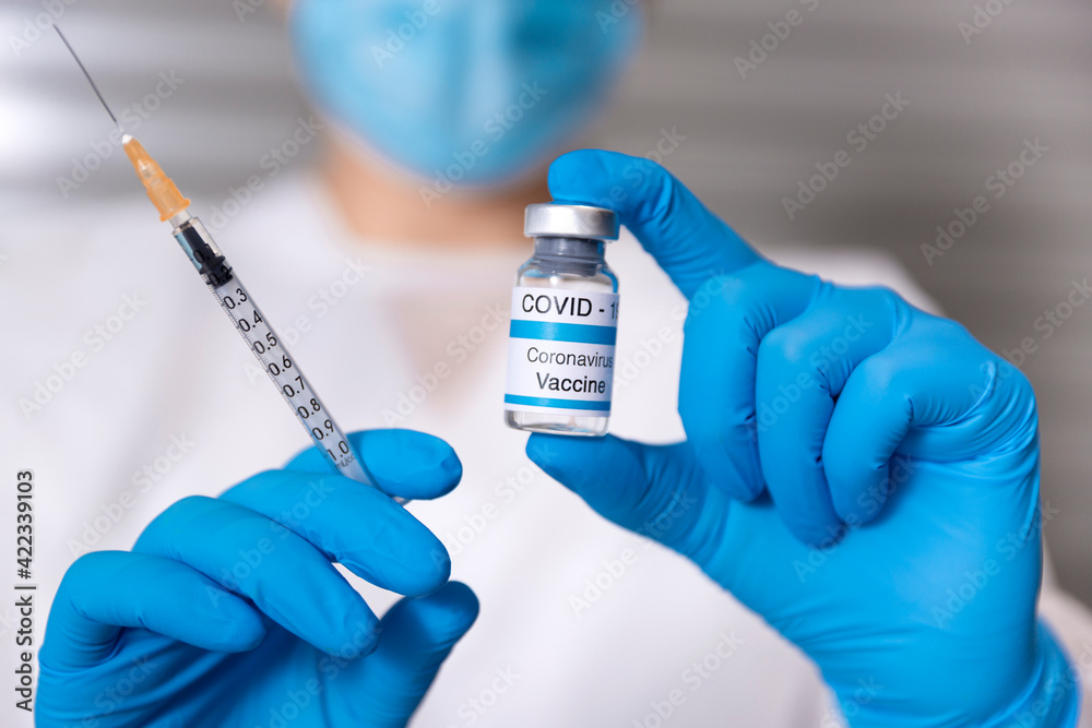 Close up of a healthcare worker wearing a medical mask and protective gloves holding a syringe and a glass vial of Covid-19 vaccine. Coronavirus vaccination concept. Selective focus. Close up of a healthcare worker wearing a medical mask and protective gloves holding a syringe and a glass vial of Covid-19 vaccine. Coronavirus vaccination concept. Selective focus.