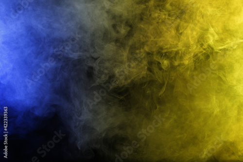 Smoke in blue yellow light on black background in darkness