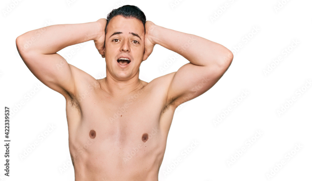 Handsome young man wearing swimwear shirtless crazy and scared with hands on head, afraid and surprised of shock with open mouth Handsome young man wearing swimwear shirtless crazy and scared with hands on head, afraid and surprised of shock with open mouth