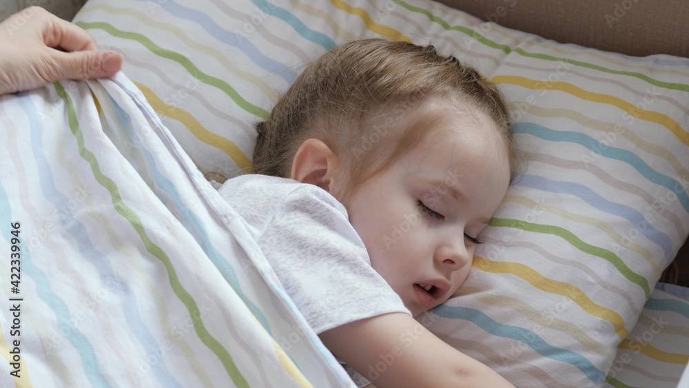 Happy baby sleeping in a crib mom covers baby with a blanket. Mom put