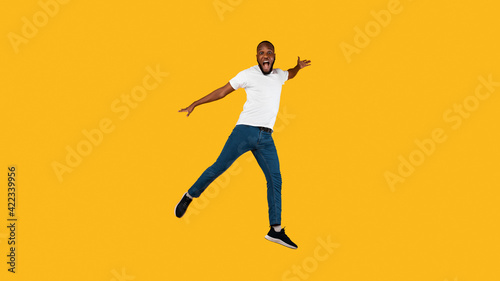 African Guy Jumping Shouting Looking At Camera, Yellow Background, Full-Length © Prostock-studio