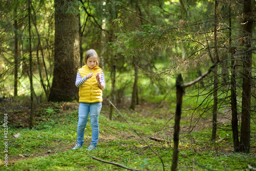 Cute young girl having fun during forest hike on beautiful summer day. Child exploring nature. Active leisure with kids. © MNStudio