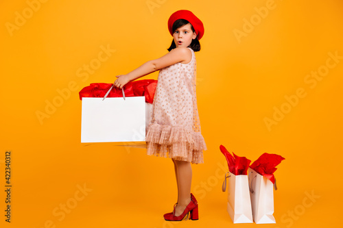 Adorbale preteen girl in mom's shoes posing with shopping bags. Studio shot of caucasian kid in dress and red beret. photo