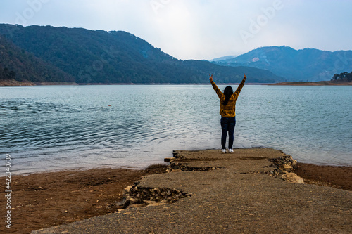 young girl in victory pose at lake shore at day from flat angle