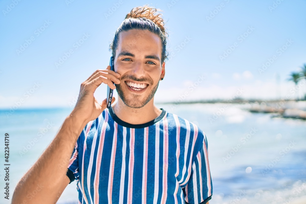 Young hispanic man smiling happy talking on the smartphone at the beach.