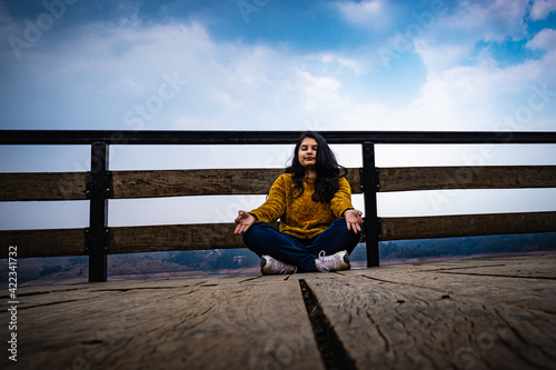 young girl meditating at wood bridge with cloudy sky from low angle leading line and space for text © explorewithinfo