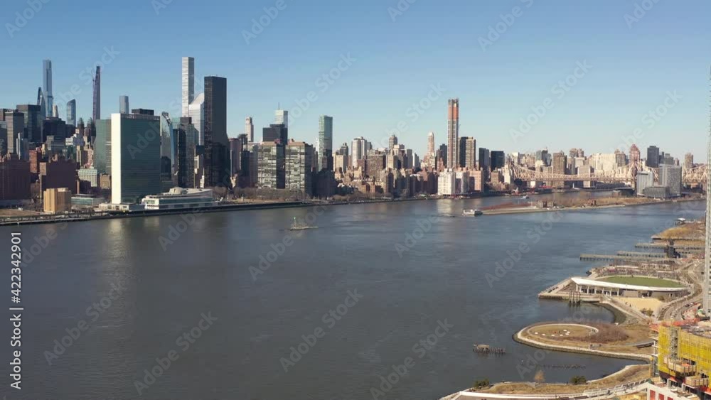 A high angle view looking north over the East River on a sunny day. The drone camera truck right, tilt up and dolly in looking up the river towards the Upper East side of Manhattan, NY