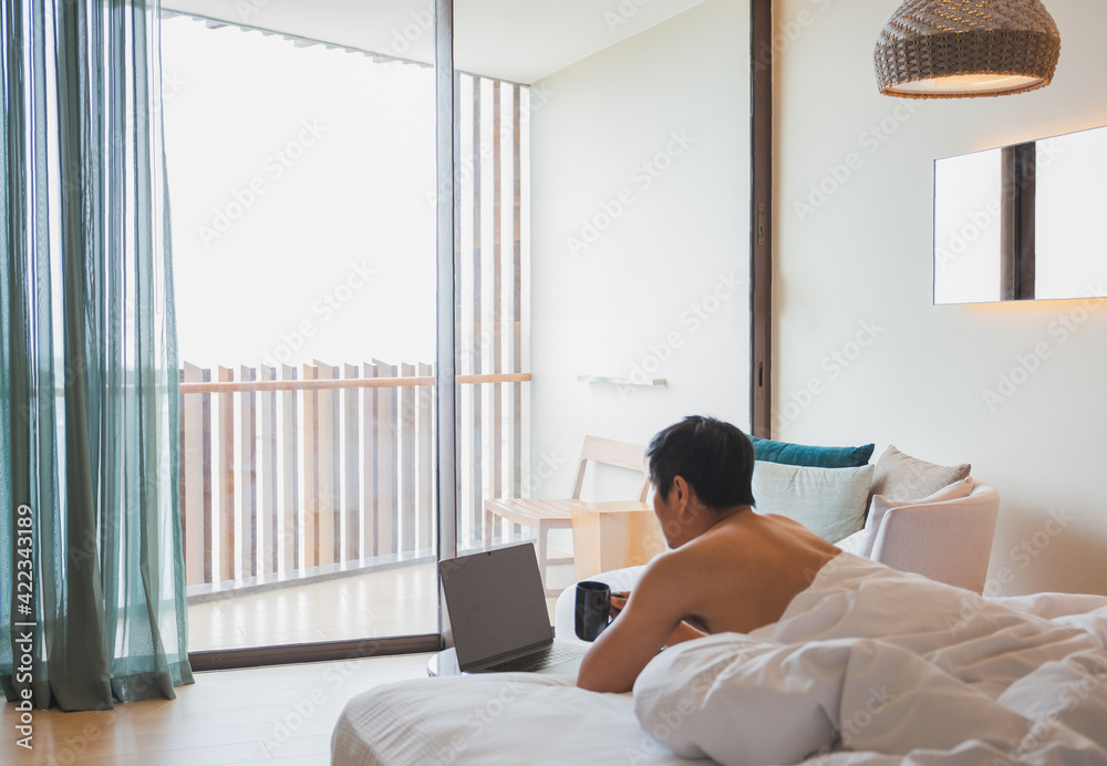 Man drinking coffee while working on laptop lying in bed. Man drinking coffee while working on laptop lying in bed.