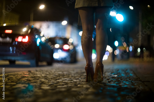 Shapely female legs in high heels on the street against the background of the lights of moving cars. photo