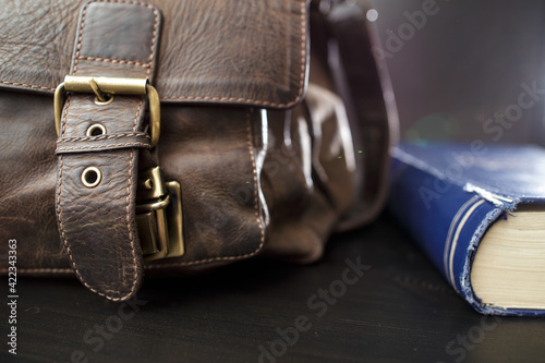 Old leather briefcase with metal buckles and a closed book lying on the table. Education concept. 