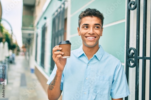 Young latin man smiling happy drinking take away coffee walking at the city.