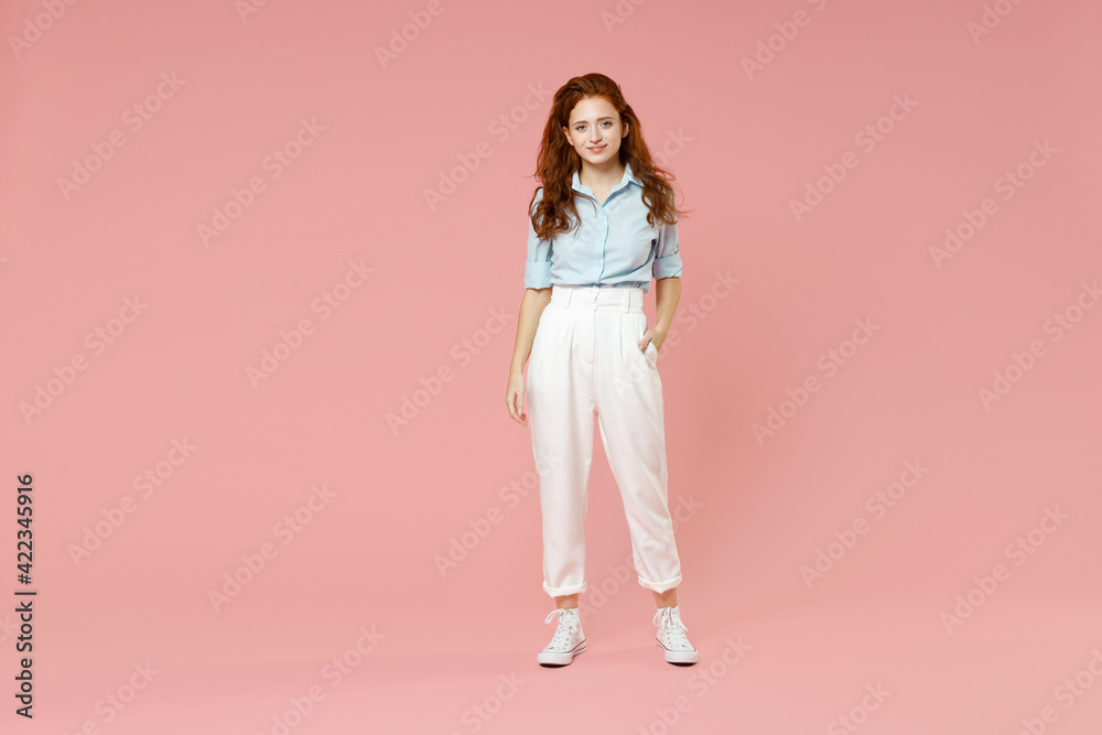 Full length body of young student positive smiling happy caucasian european redhead woman 20s wearing blue shirt pants standing looking camera isolated on pastel pink color background studio portrait. Full length body of young student positive smiling happy caucasian european redhead woman 20s wearing blue shirt pants standing looking camera isolated on pastel pink color background studio portrait.
