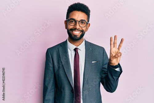 Handsome hispanic business man with beard wearing business suit and tie showing and pointing up with fingers number three while smiling confident and happy.