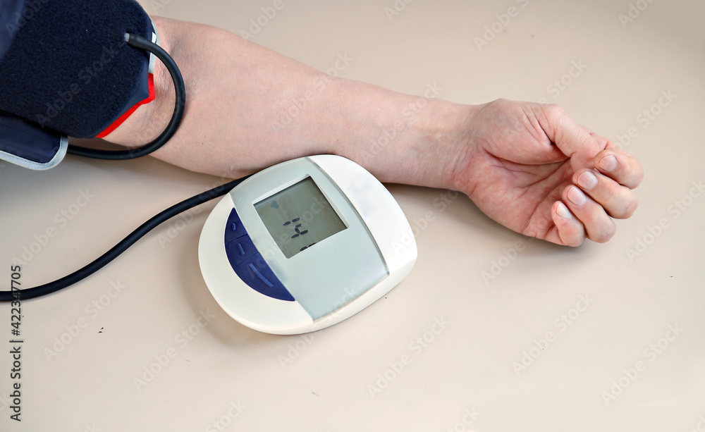 Tonometer measures blood pressure in man. Hand with device is on gray table Tonometer measures blood pressure in man. Hand with device is on gray table
