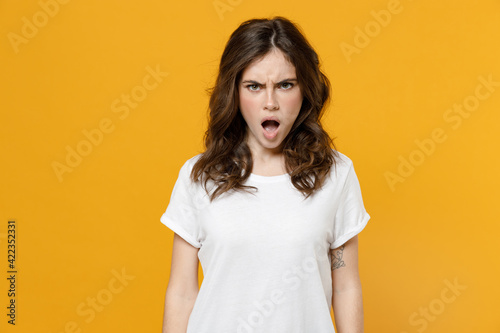 Obraz na płótnie Young shocked impressed angry indignant scared student woman 20s in white basic blank print design casual t-shirt look camera with opened mouth isolated on yellow orange background studio portrait