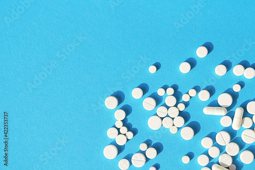 White tablets, pills and capsules on a sky-blue background with space for text. Medical background. photo