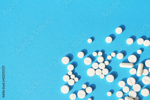 White tablets, pills and capsules on a sky-blue background with space for text. Medical background.