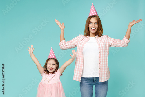 Happy woman in pink clothes birthday hat have fun child baby girl 5-6 years old. Mom little kid daughter raised up hands celebrate isolated on blue background studio. Mother's Day love family concept.