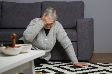 Senior woman lying on the floor in living room. Woman fell on the floor because of heart attack, dizziness, faint or accident. Weak elderly woman with walking stick trying to get up.