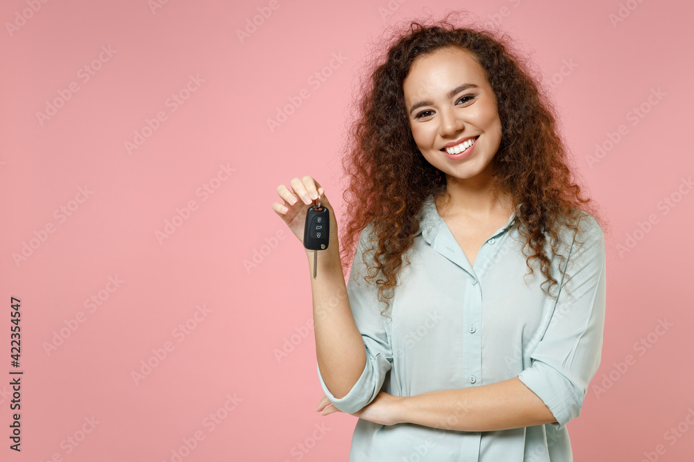 Young black african american fun smiling satisfied happy curly female driver woman 20s wear casual blue shirt holding car key looking camera isolated on pastel pink color background studio portrait Young black african american fun smiling satisfied happy curly female driver woman 20s wear casual blue shirt holding car key looking camera isolated on pastel pink color background studio portrait