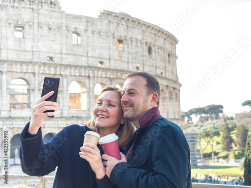 Couple of young people drinking coffee and taking a selfie at the Colosseum