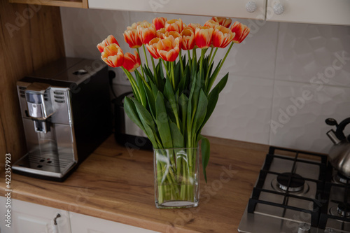 Bouquet of bright tulips in the kitchen. Tulips on the background of a coffee machine. Spring flowers. Fresh orange buds