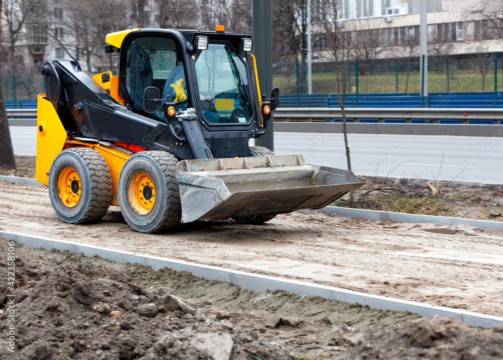 Little nimble road grader in motion on a sidewalk under construction in a light blur against the background of a city road.