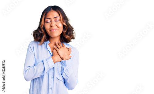 Young beautiful mixed race woman wearing casual business shirt smiling with hands on chest with closed eyes and grateful gesture on face. health concept.
