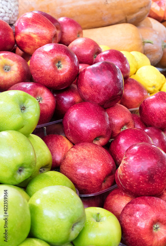 Red and green apples are stacked in a heap on the market counter and attract the attention of buyers.