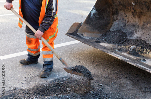 A road service worker cleans a bad section of the road with a shovel.