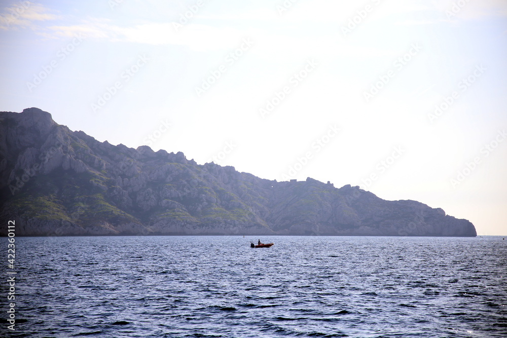 Boat with silhouette of people and background of the rocky coast lined with trees, Parc National des Calanques, Marseille, France