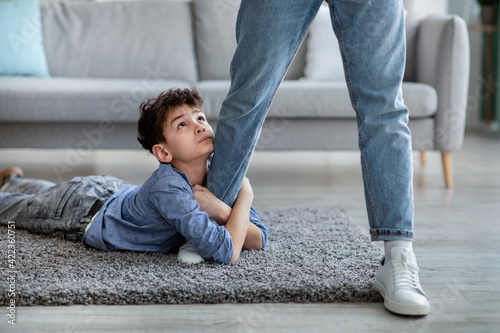 Please stay  dad. Sad little boy embracing his father leg and looking up