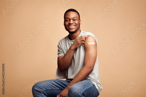 Leinwand Poster Covid-19 Vaccinated African Man Showing Arm With Plaster, Beige Background
