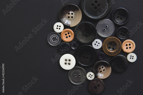 Many round buttons of different sizes on a black background, top view. Needlework and sewing concept. Handicraft goods store.