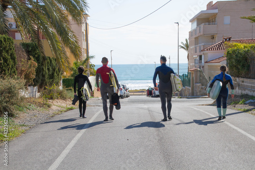 Four spanish surfers people walking in the street of a mediterranean beach with surfboards looking at waves in Alicante.