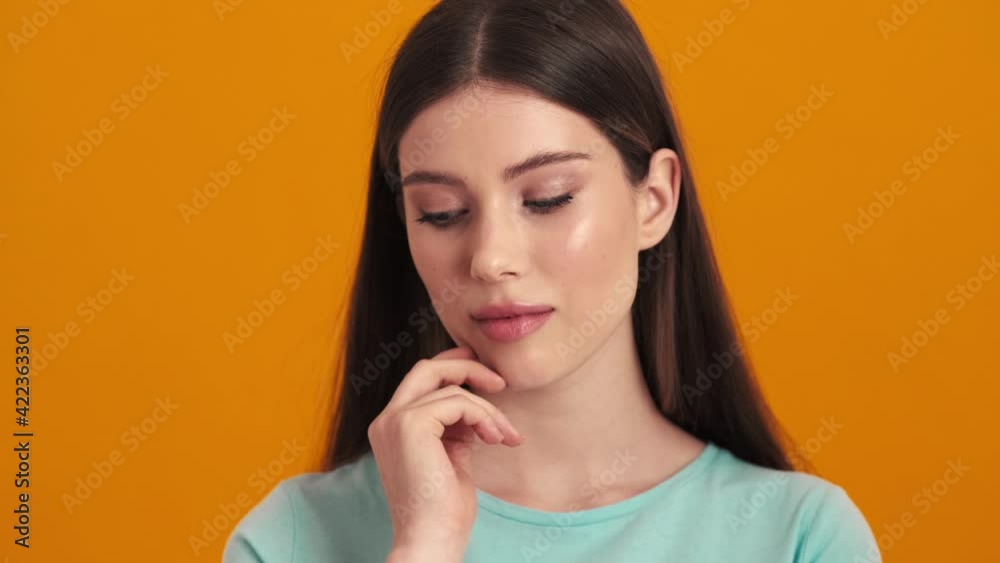 A thinking young woman is posing standing isolated over orange background in the studio A thinking young woman is posing standing isolated over orange background in the studio