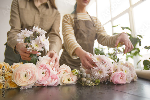Close up of flowers on table in flower shop with two female florists arranging bouquets, copy space photo