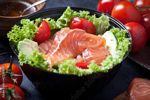fresh salmon salad with avocado and lettuce leaves, sauce and fresh cherry tomatoes, closeup