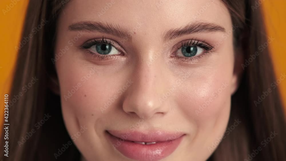 A close-up view of a beautiful young woman is looking to the camera standing isolated over an orange background in the studio A close-up view of a beautiful young woman is looking to the camera standing isolated over an orange background in the studio