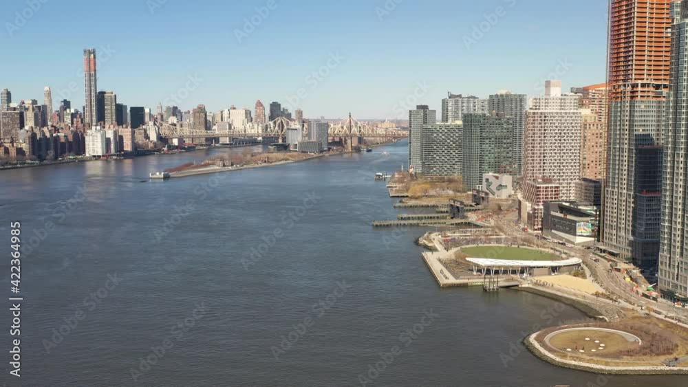 A high angle view looking north over the East River on a sunny day. The drone camera truck right and pan left, looking up the river to the Upper East side of Manhattan.