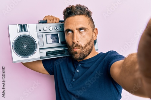 Handsome man with beard holding boombox, listening to music making fish face with mouth and squinting eyes, crazy and comical.