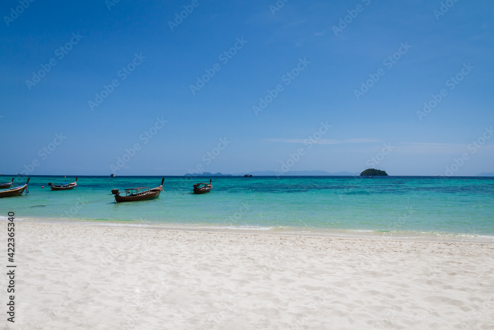White sand beach, clear blue sky and clear turquoise sea water with traditional style transport long-tail boat parking in the sea. Summer of Andaman sea, Southern of Thailand.