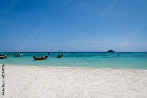 White sand beach, clear blue sky and clear turquoise sea water with traditional style transport long-tail boat parking in the sea. Summer of Andaman sea, Southern of Thailand.