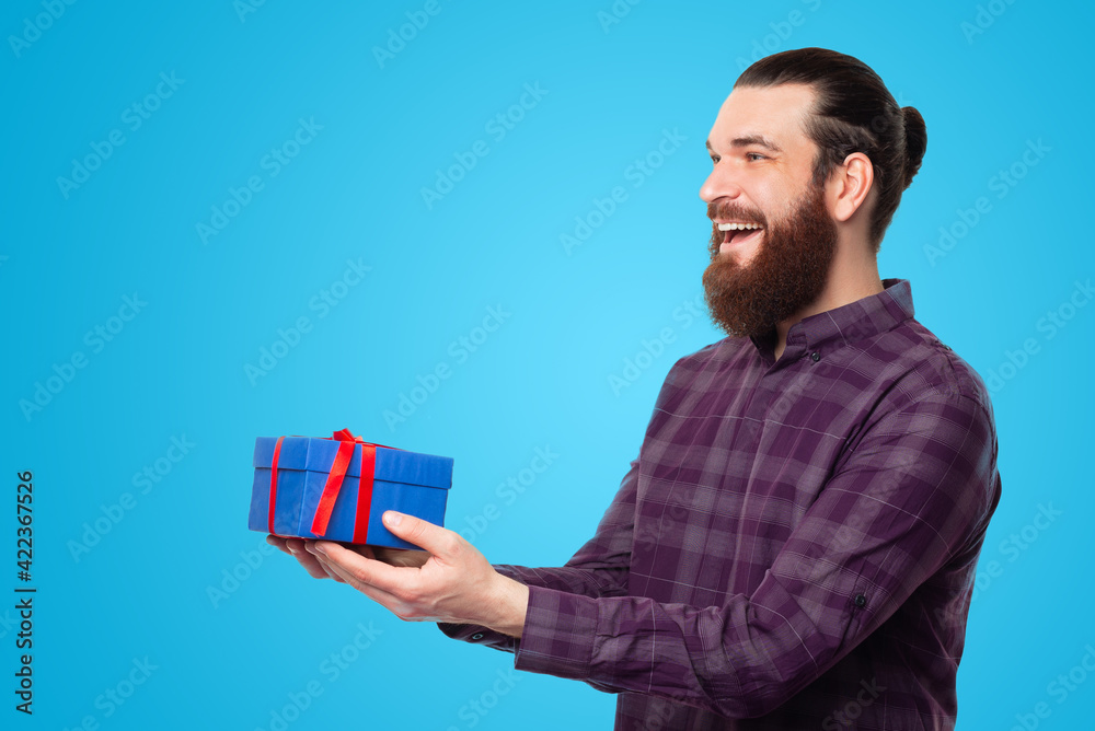 Joyful young man with beard giving a gift box to someone