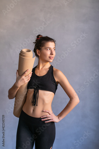 Woman standing at work out or yoga class with fitness mat in her hads. Copy space on dark background