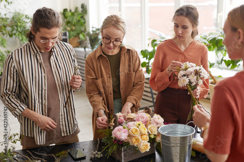 Diverse group of young people arranging flowers in florists workshop while attending class on floral art